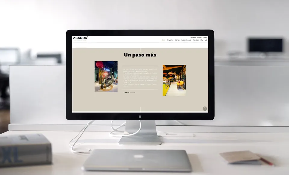 Rediseño web de Abanda en un monitor de oficina con el titular «Un paso más» y fotos de un local