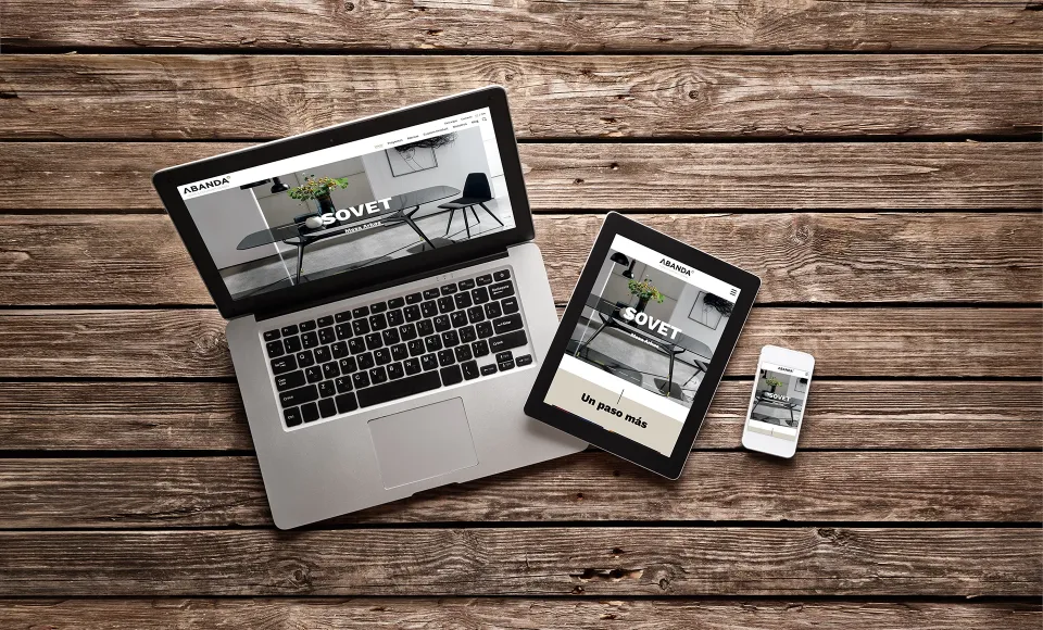 Web de Abanda en portátil, tablet y móvil sobre una mesa de madera, con la marca Sovet