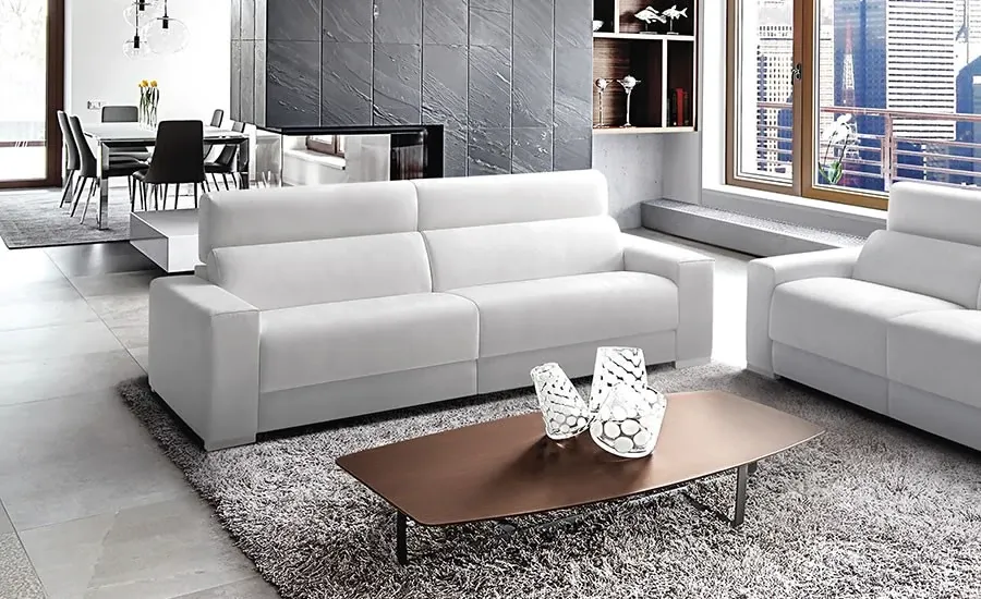Sofá de piel blanca en un salón con mesa de centro oscura y zona de comedor al fondo