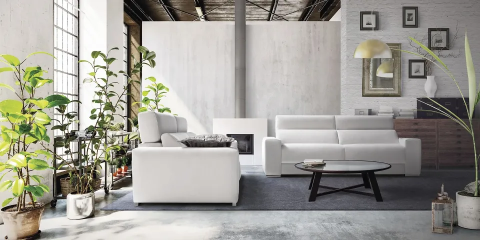 Salón de estilo industrial con sofás blancos, plantas y una mesa de centro redonda de cristal