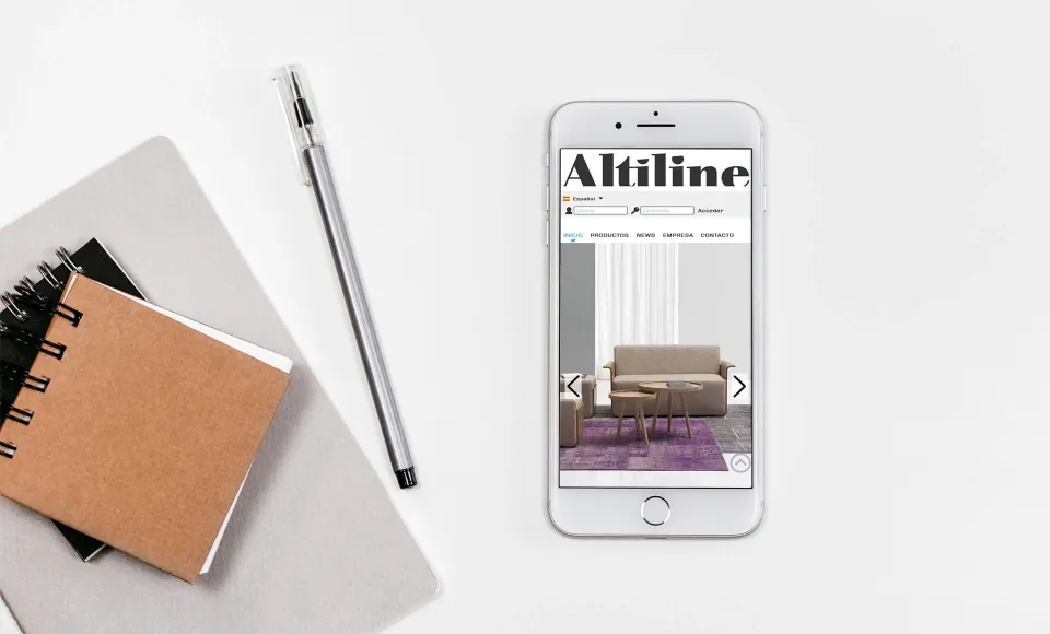 Web de Altiline en un móvil con la ficha de un sofá beige, junto a una libreta y un bolígrafo