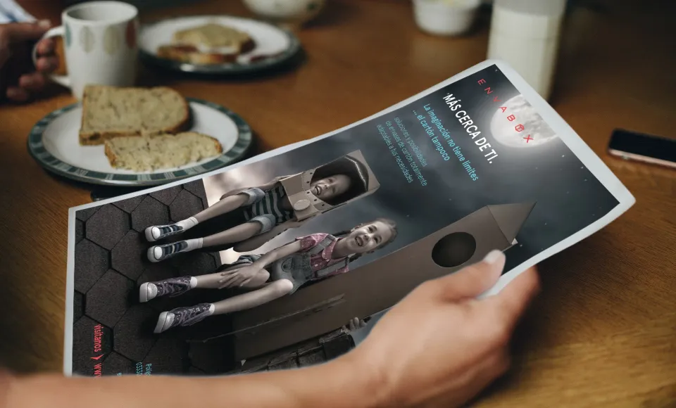Mano sosteniendo una revista de Envabox abierta junto a un desayuno sobre la mesa
