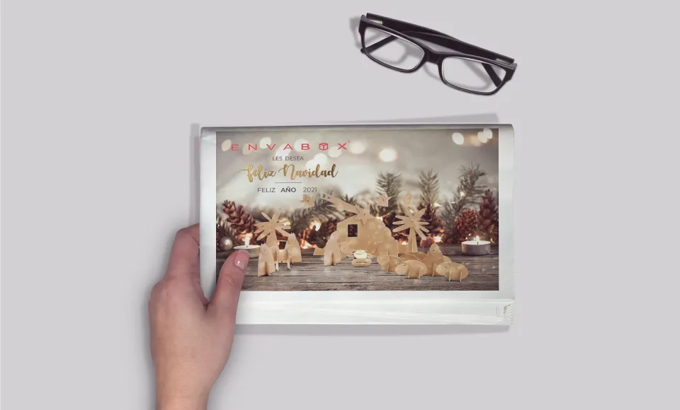 Mano sosteniendo un folleto navideño de Envabox con renos de cartón y luces