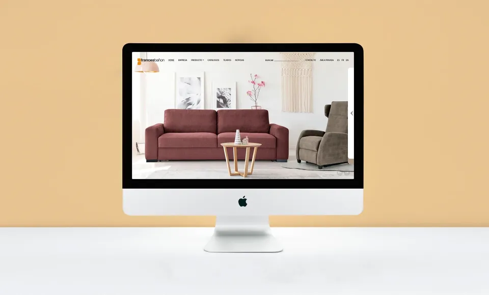 Web de Francés Bañón en un iMac con un sofá granate en la página de inicio y fondo naranja