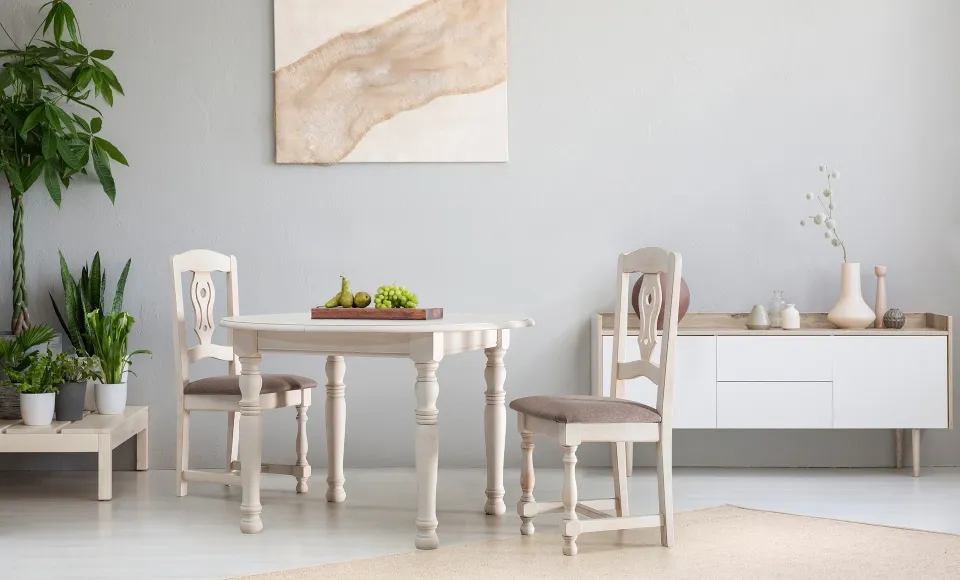 Wooden dining table with two carved chairs, a painting and a white sideboard