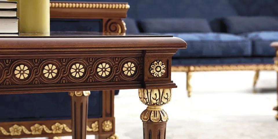 Close-up of a carved wooden table with gilded rosettes beside a blue sofa