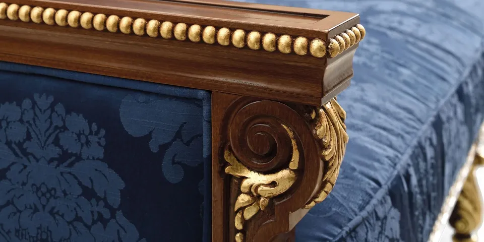 Close-up of the carved, gilded arm of a sofa with patterned blue upholstery
