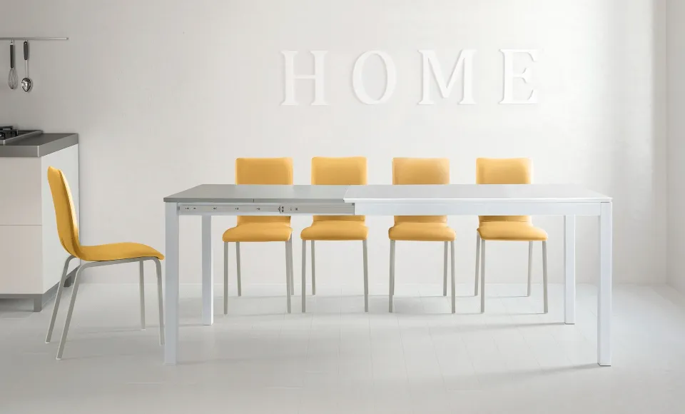 Comedor blanco con una mesa y sillas amarillas de Tabou, y letras HOME en la pared