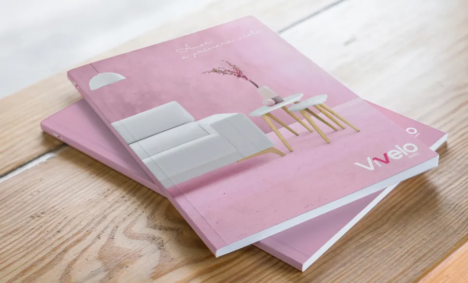 Catálogos de Vívelo apilados sobre una mesa de madera, con portada rosa e ilustración de un sillón blanco