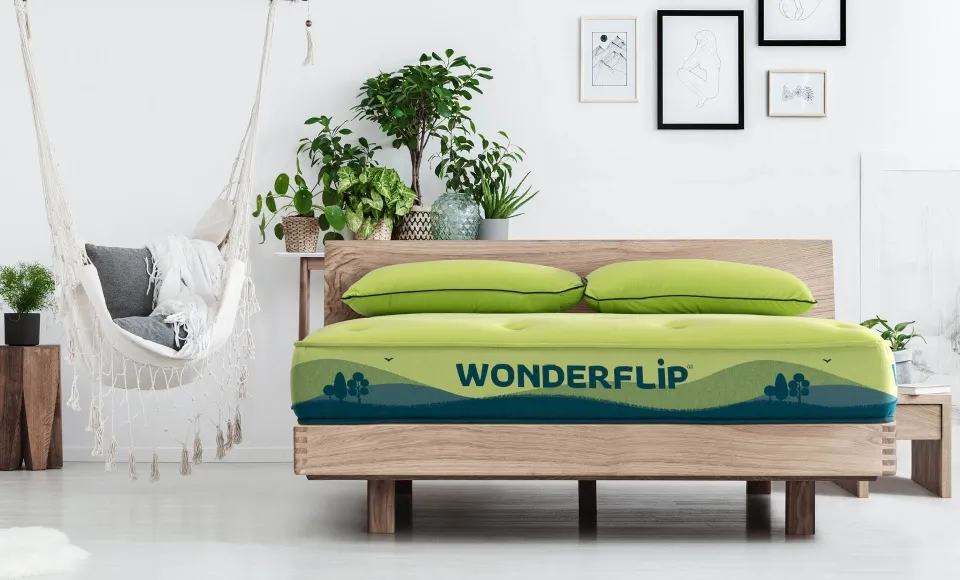 Green Wonderflip mattress on a wooden bed base, in a bedroom with plants and a hanging chair