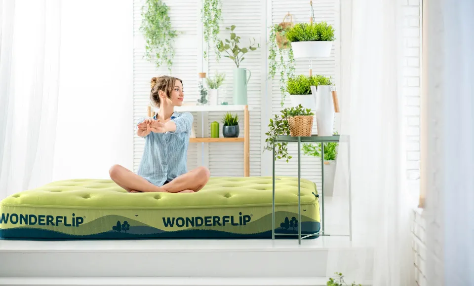 Woman sitting and stretching on the green Wonderflip mattress, surrounded by plants