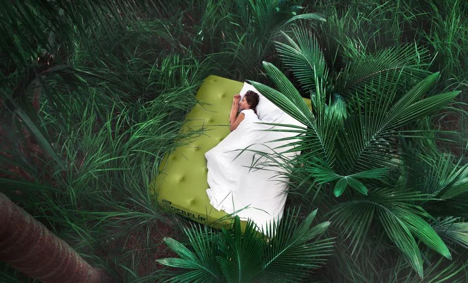 Aerial view of a person sleeping on the Wonderflip mattress amid dense jungle foliage
